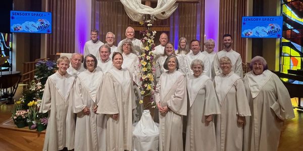 Choir group dressed in white robes posing inside a church.