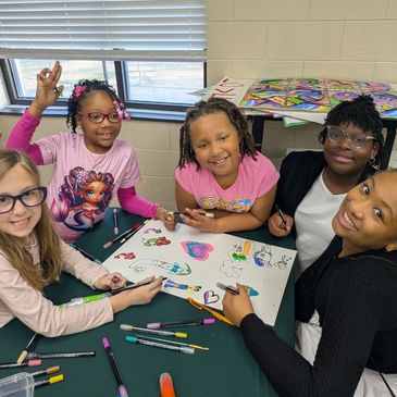 Group of kids drawing and smiling at a table.