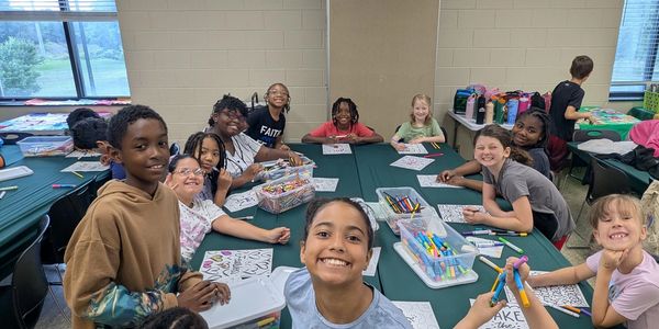 Group of children smiling and coloring around a table.