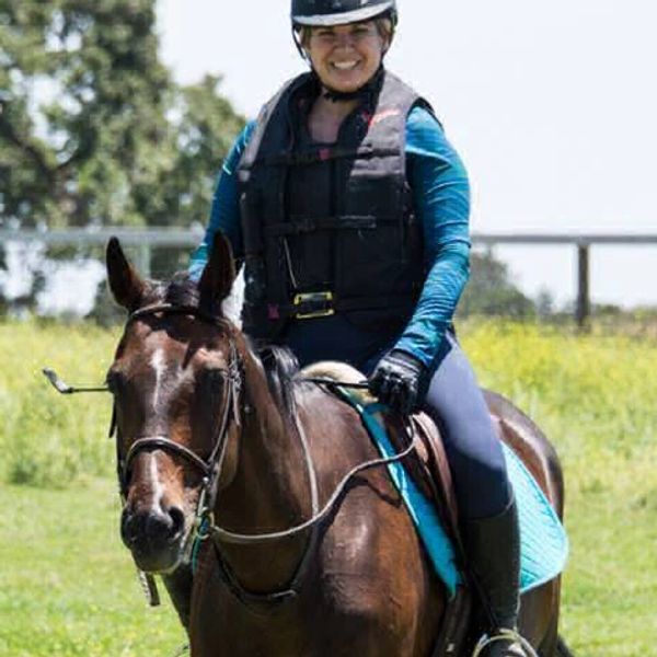 Sarah Rune riding a lovely bay horse, wearing cross-country safety gear, with beautiful green fields
