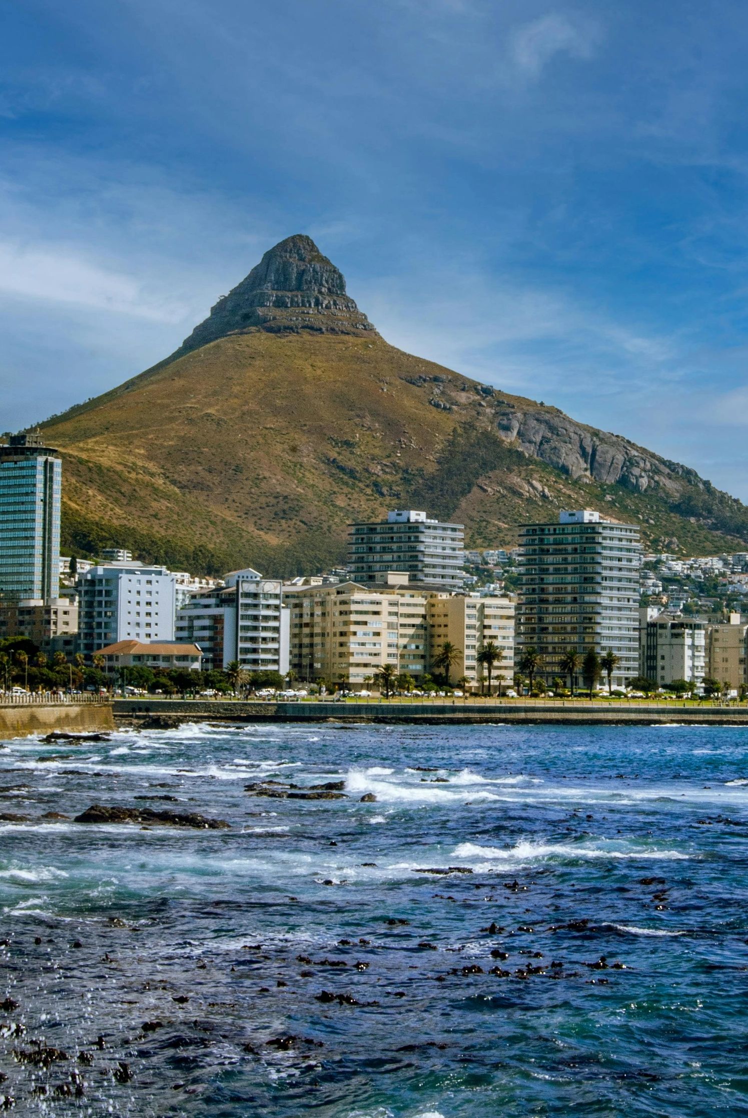 Coastal cityscape with a prominent mountain and ocean waves.