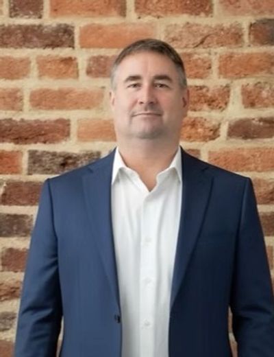 Man in blue suit standing against a brick wall.