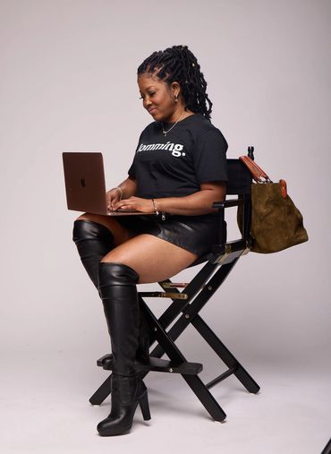 Woman in black leather boots and skirt working on a laptop while seated.
