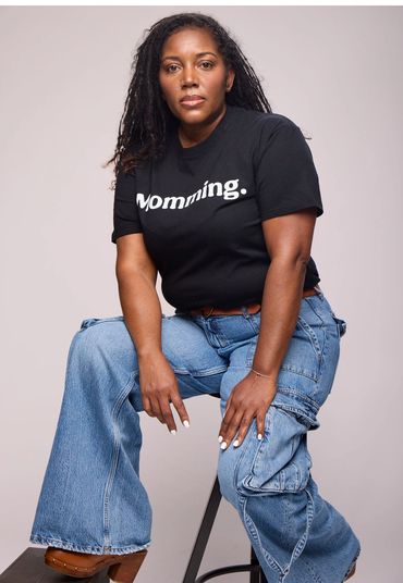 Confident woman wearing a black "Momming." t-shirt and wide-leg jeans.