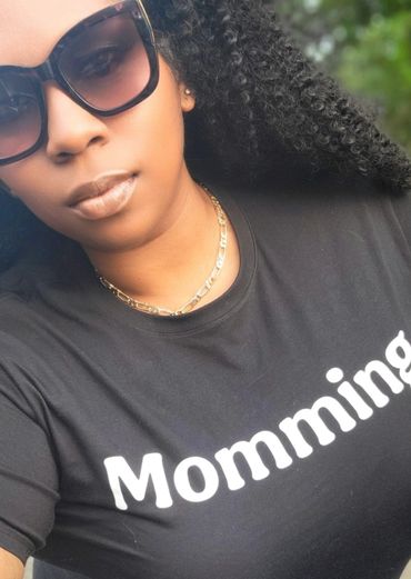 Woman wearing sunglasses and a black shirt with 'Momming' text.