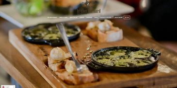 A wooden board with two small pans of creamy spinach dip and toasted bread slices.