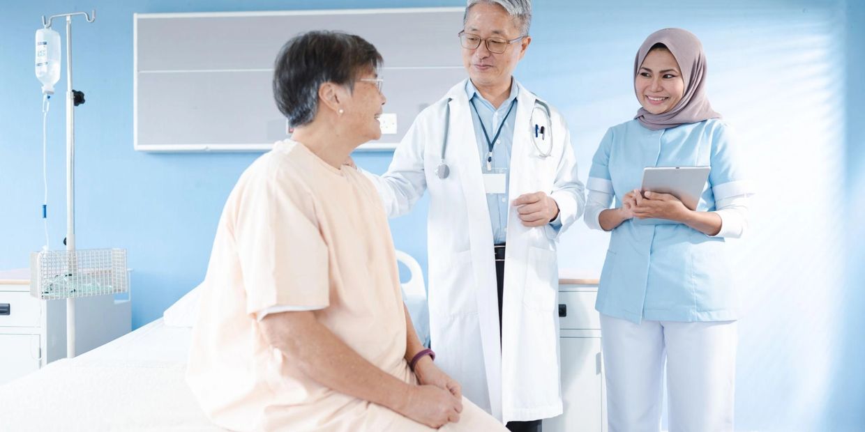 Doctor and nurse consulting a smiling elderly patient in a hospital room.