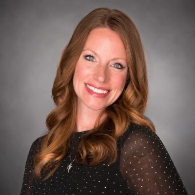 Smiling woman with red hair in a black dotted blouse.