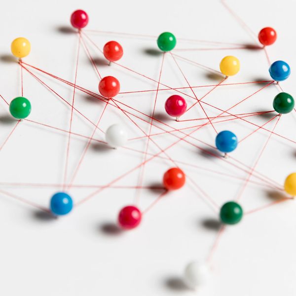Colorful push pins connected by red thread on white surface.