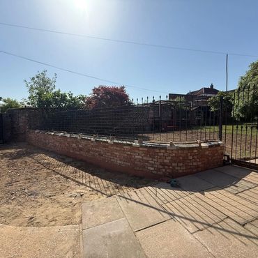 Newly built brick and iron fence around a garden.