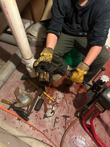 Person unclogging drain with a dirty clog in a basement.