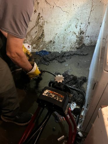 Person using a drain snake to clear a flooded basement floor.