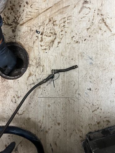 A gloved hand working on a dirty floor drain with a plumbing snake nearby.