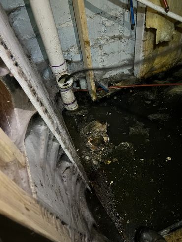 Dirty and clogged basement drain pipes with standing water and debris.
