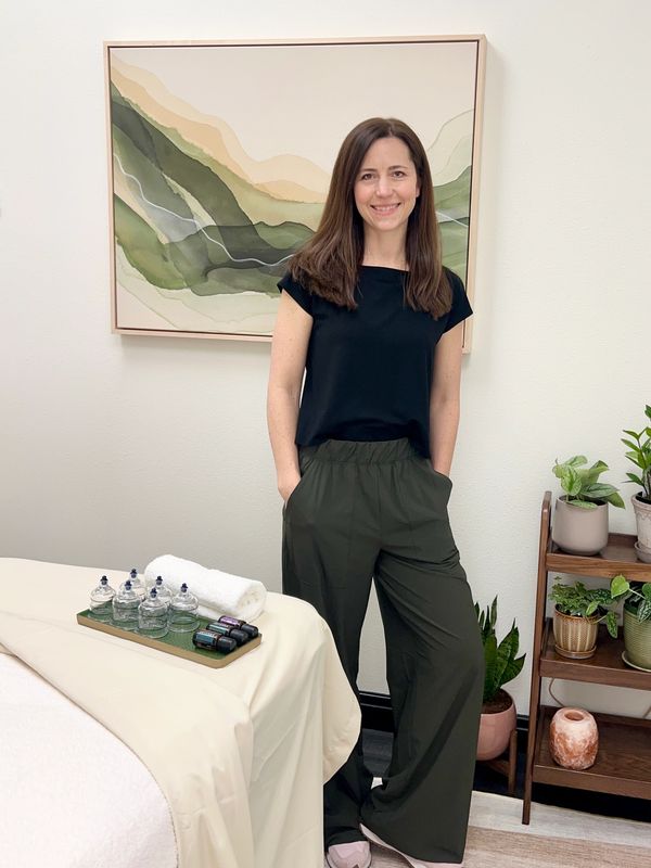A woman stands smiling in a calm, plant-filled wellness room.
