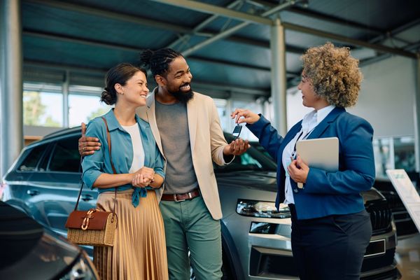 A couple receives car keys from a saleswoman in a car dealership