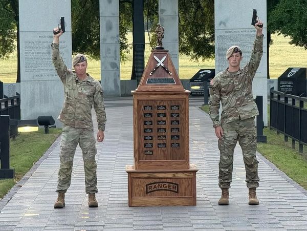 Two individuals in U.S. Army Ranger uniforms holding pistols aloft next to a "Ranger" trophy.