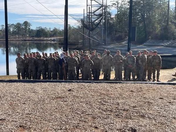 A large group of individuals in U.S. Army uniforms standing outdoors near a body of water.
