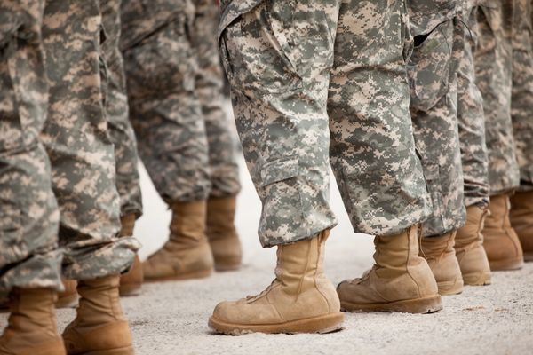 A close-up of several individuals wearing camouflage military pants and tan boots.