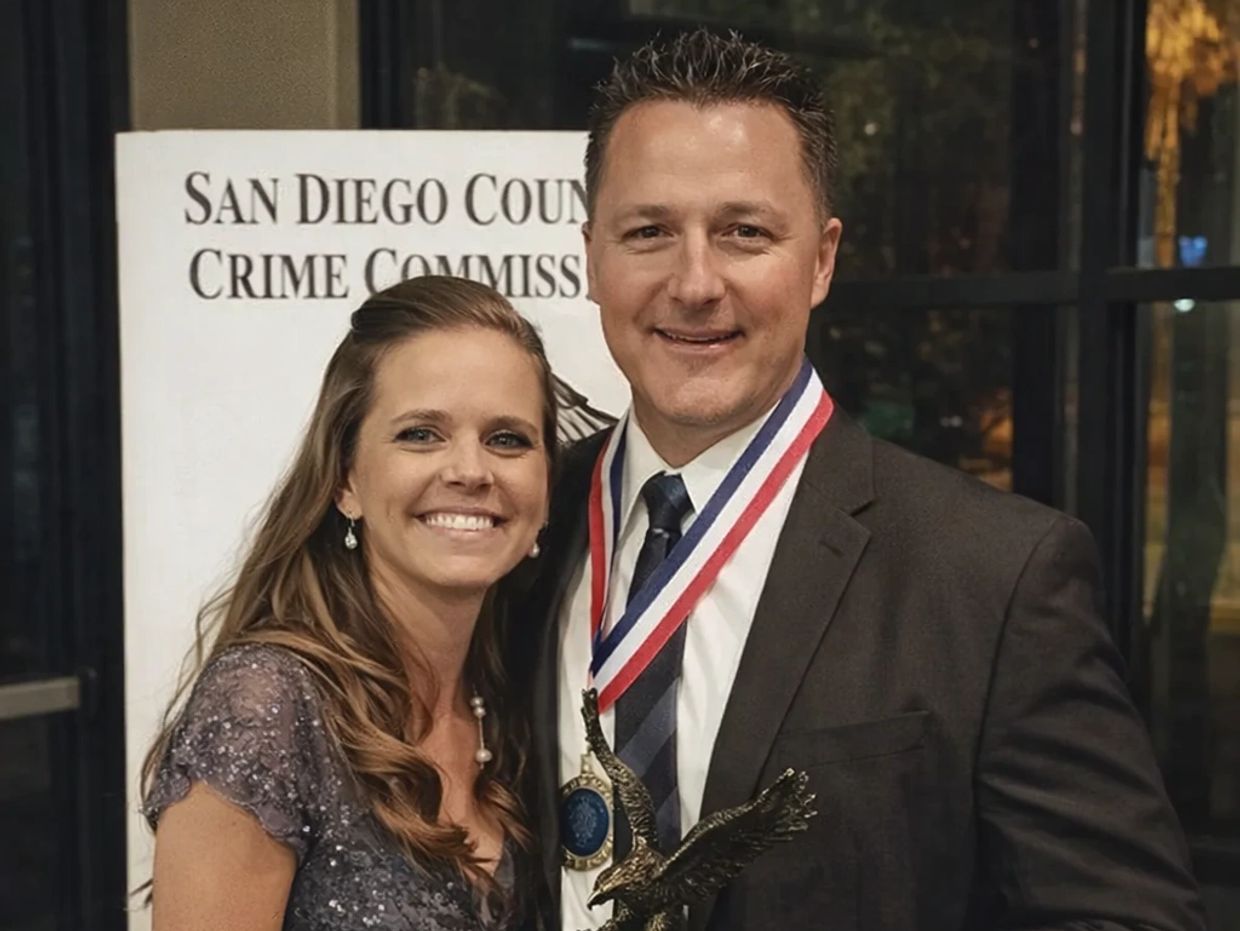 Couple smiling at a San Diego County Crime Commission event with an award and medal.