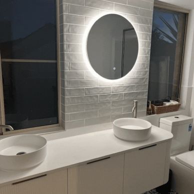 Modern bathroom with dual sinks and a glowing round mirror.