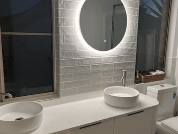 Modern bathroom with dual sinks and a glowing round mirror.