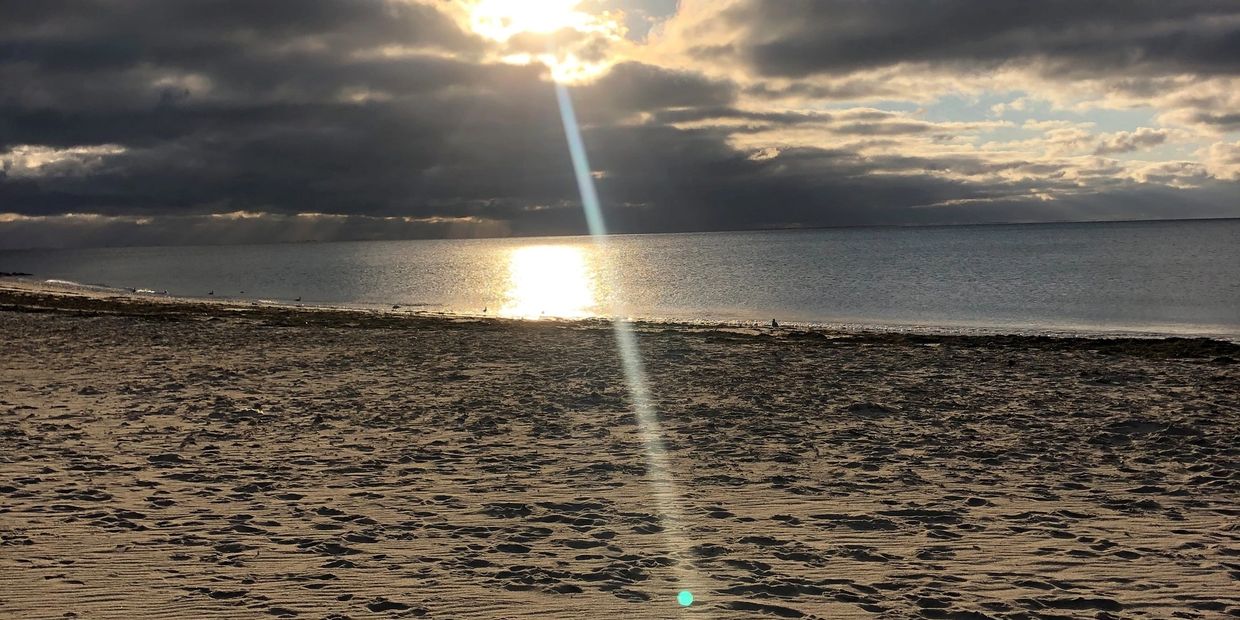 Sunlight breaks through clouds onto a peaceful beach at sunset.