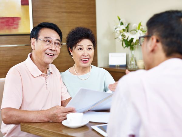 An older couple sits at a table, holding documents and smiling during a discussion with a man.