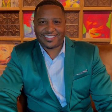 Smiling man in a green blazer sitting indoors.