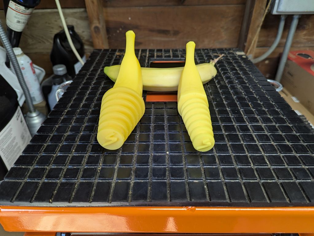 Two yellow spiral objects resembling bananas on a black grid surface with a real banana behind.