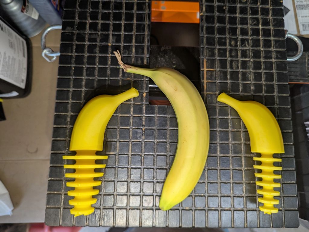 A banana flanked by two yellow plastic banana-shaped objects on a black surface.