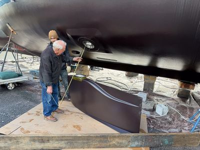 Two men measuring the hull of a boat on dry dock.