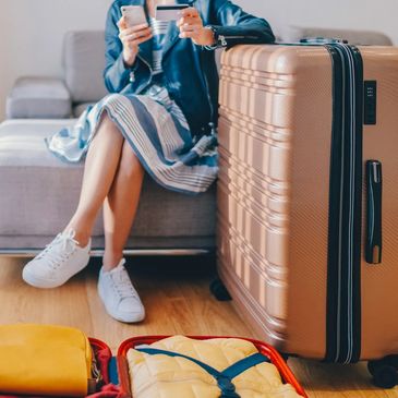Woman sitting on a couch with a suitcase, holding a phone and credit card.