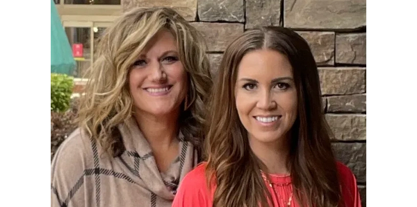 Two women smiling in front of a stone wall.