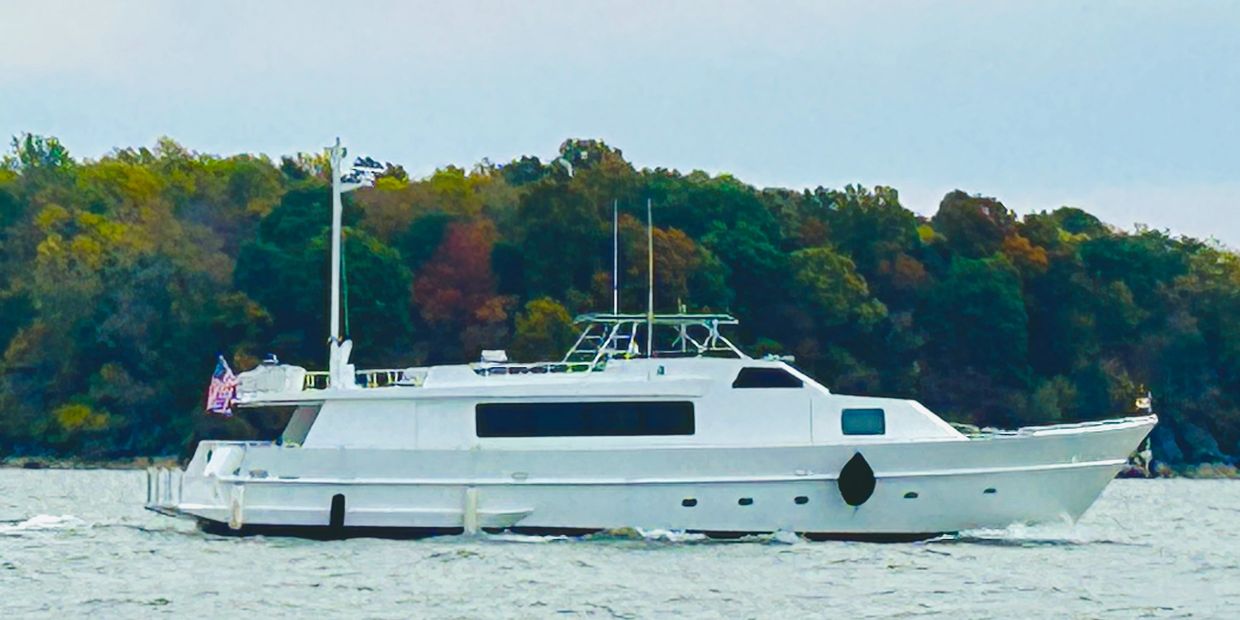 A white yacht cruising on a lake with a forested shore in the background.