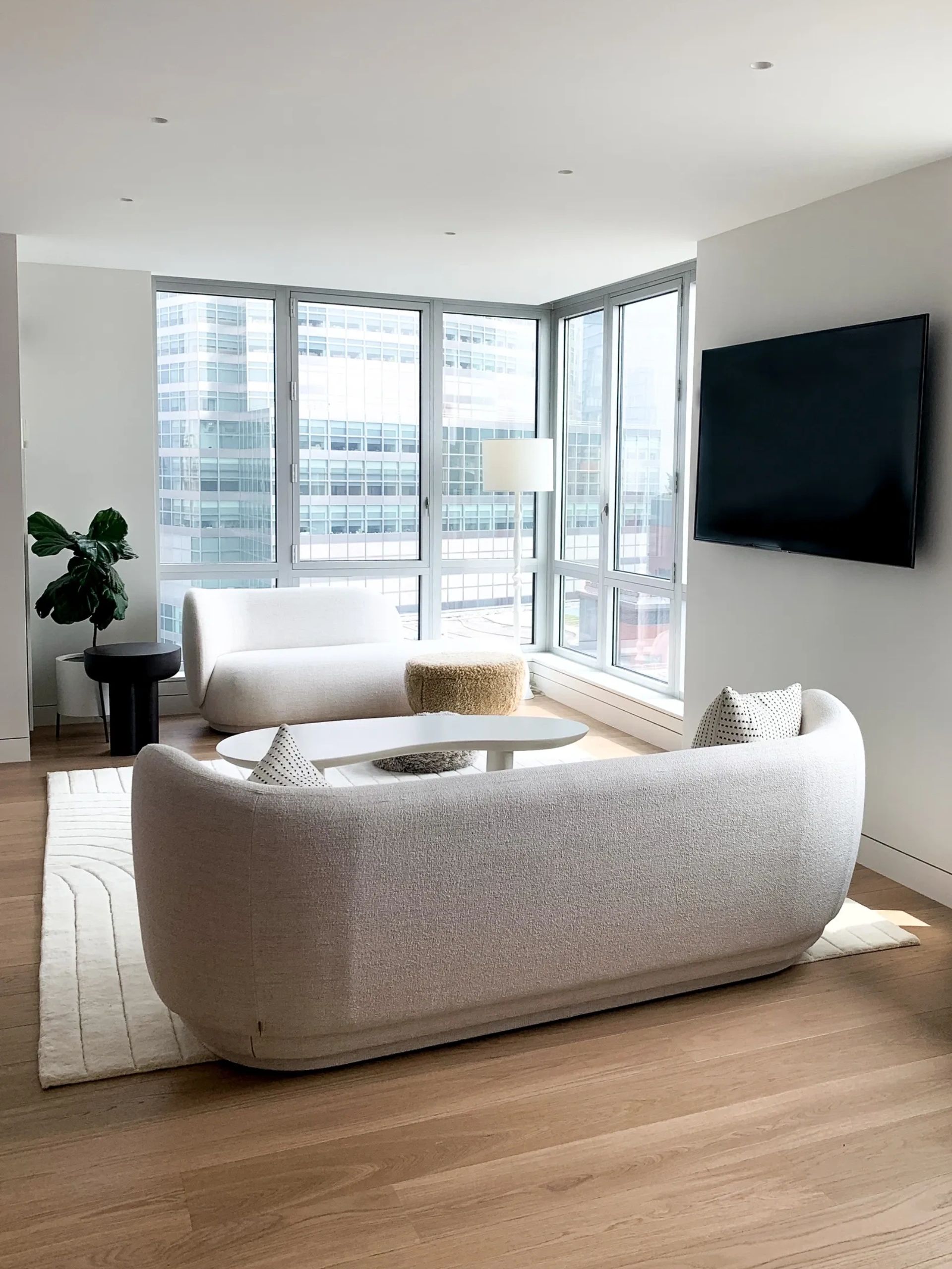 Modern living room with white curved sofas and large windows.