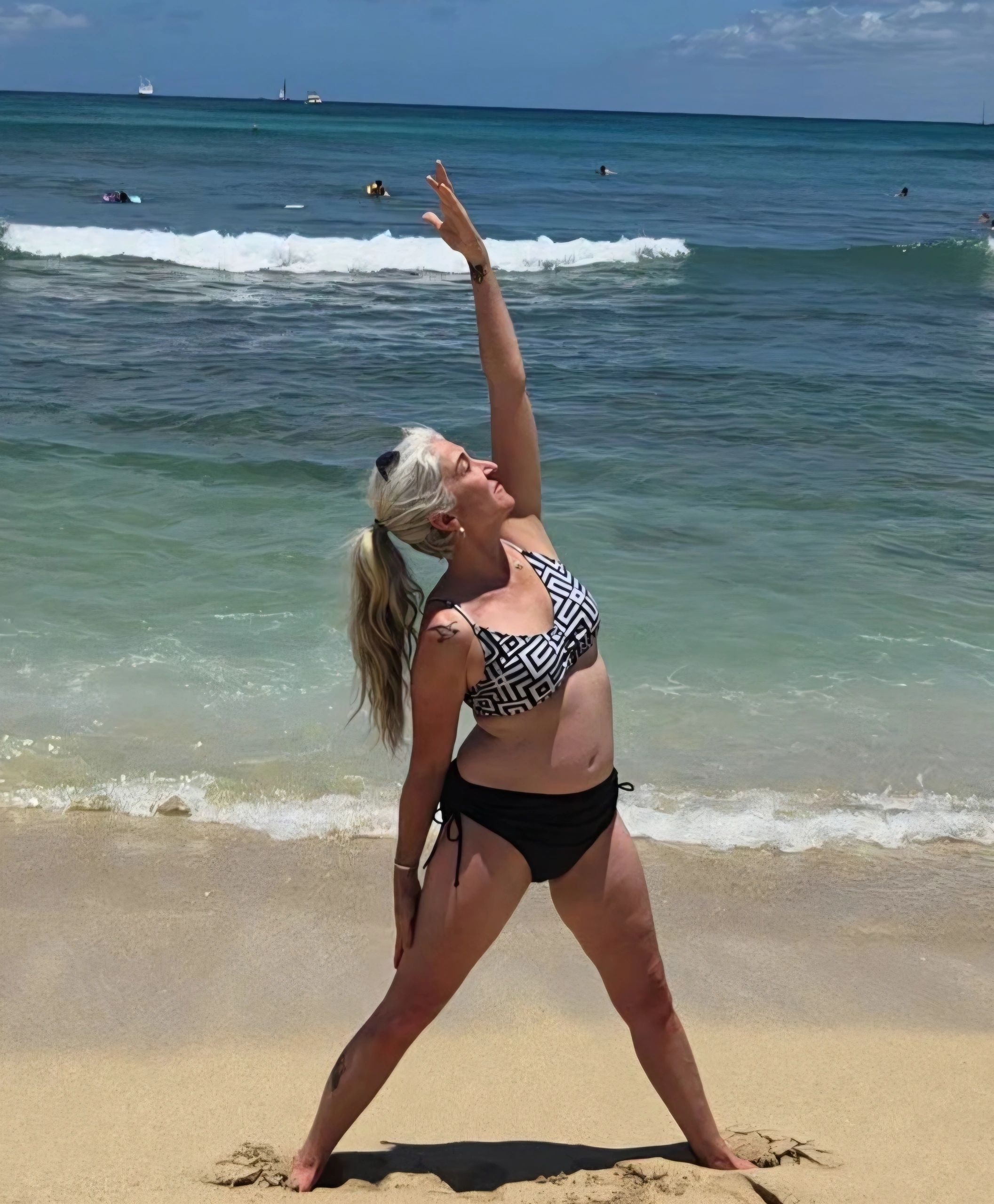 Woman on beach wearing black and white bikini doing a yoga pose called reverse triangle