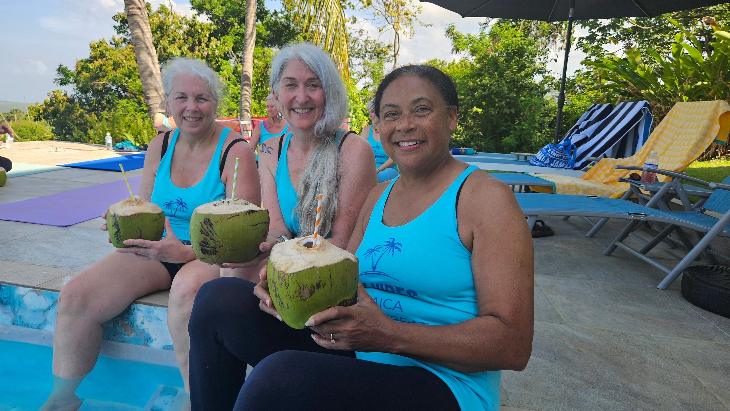 3 women sitting by a pool holding coconuts