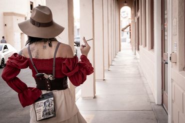 Woman in vintage attire with a gun holstered and smoking a cigarette.