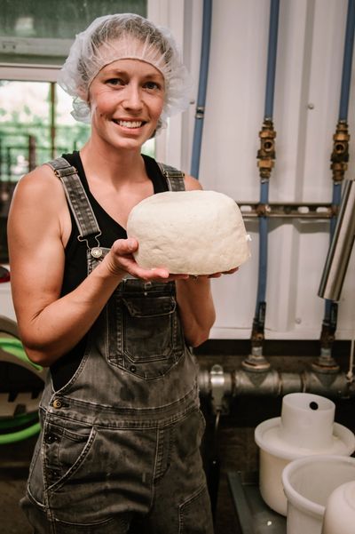 Woman in overalls holding a large block of fresh cheese.