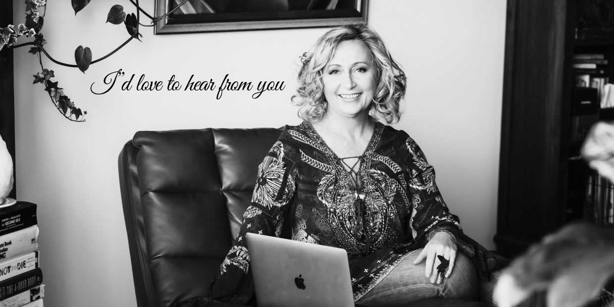 Smiling woman sitting on a leather chair with a laptop, surrounded by books and plants.