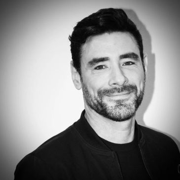 Smiling man with facial hair in black and white photo.