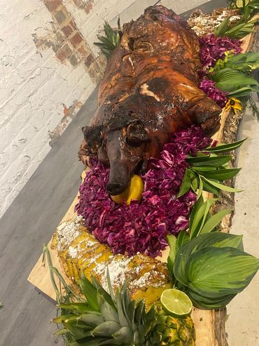 Whole roasted pig garnished with purple cabbage, pineapple, and leafy greens on a wooden board.
