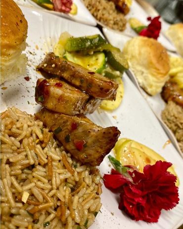 A delicious meal with rice, glazed meat, vegetables, and a roll, garnished with a red flower.