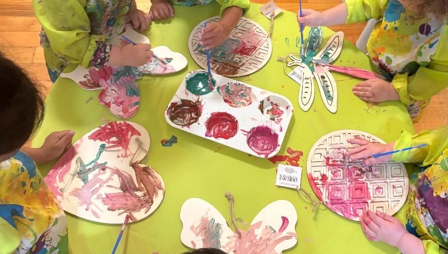 Children painting colorful designs on paper crafts around a table.