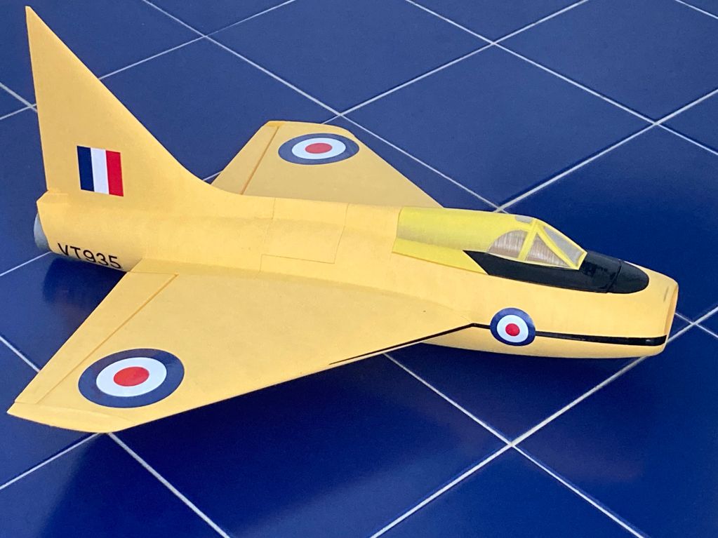 Yellow model jet airplane with British roundels on blue tiled surface.