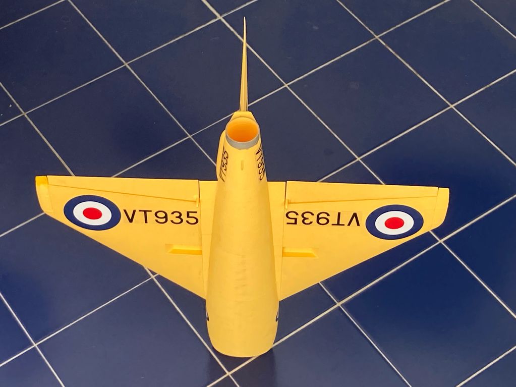 Top view of a yellow model airplane with VT935 markings on a tiled floor.