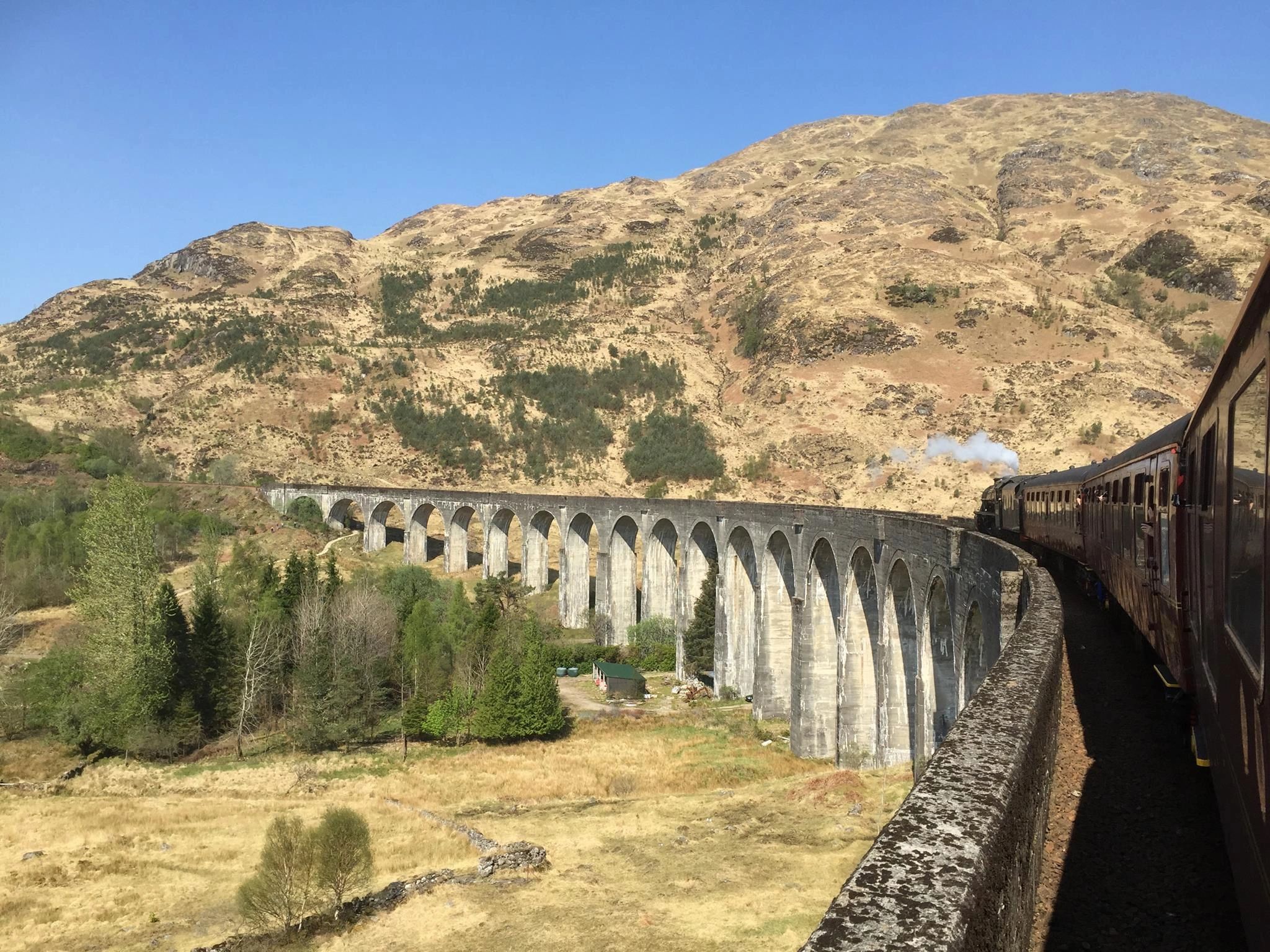 The jacobite Steam Train travelling over Glenfinnan Viaduct or harry Potter bridge and blue skies