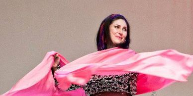 A dark-haired dancer with a pink scarf smiles while looking to the side