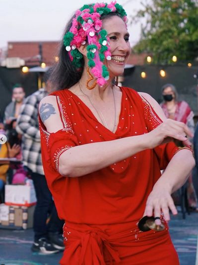 A person in a red costume and wearing finger cymbals smiles while dancing